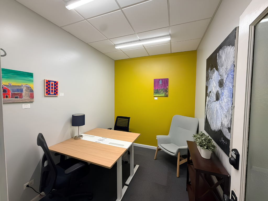 Private FlexDesk office with shared desk, lounge chair, and bright yellow accent wall at Prism Spaces